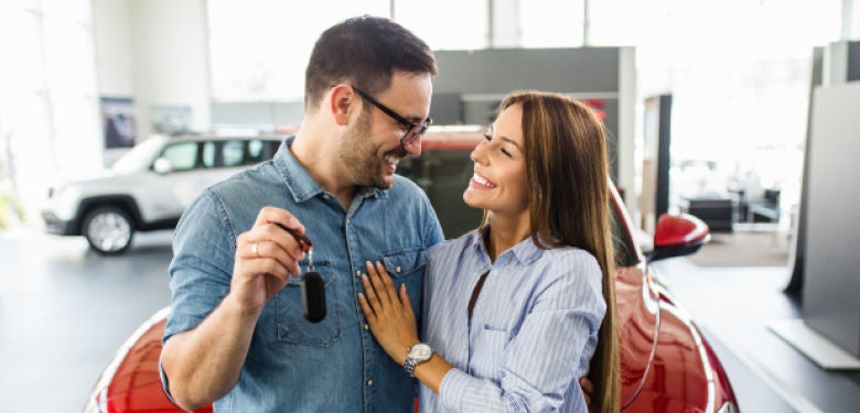 Smiling couple infront of new red car